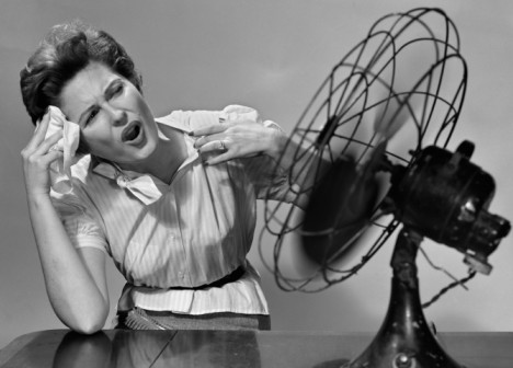 AAN3PY 1950 1950s WOMAN SITTING IN FRONT OF FAN WIPING FOREHEAD VERY HOT